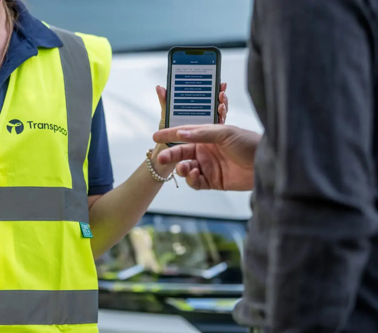 Transpoco employee in a high-vis jacket showing vehicle telematics data to a driver on a smartphone