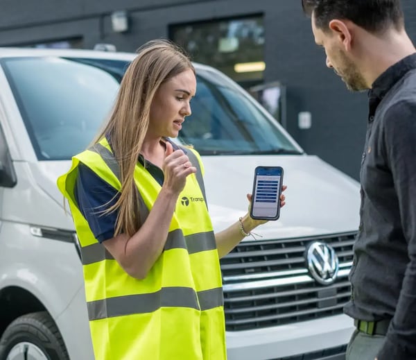 Transpoco employee holding a mobile phone, showing a driver in a black shirt vehicle telematics data