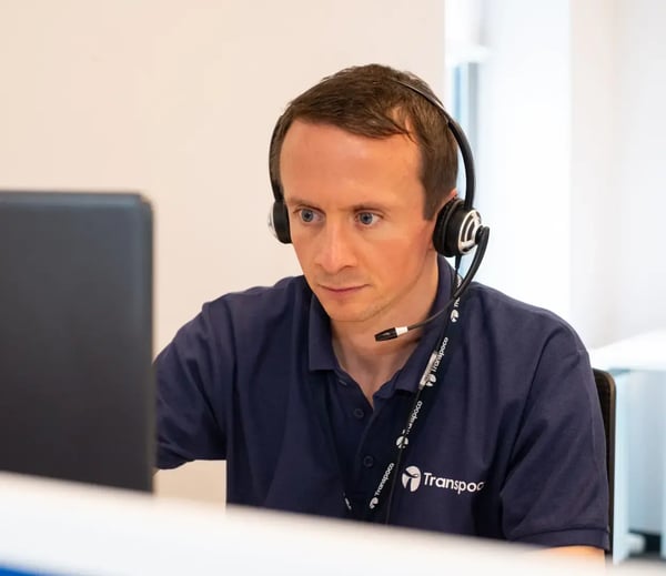 Transpoco employee in a dark blue shirt, wearing a headset and sitting in front of his computer