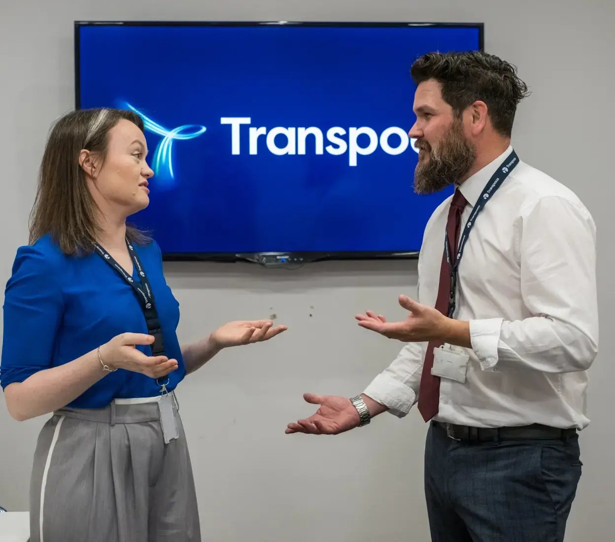 Two Transpoco employees talking in front of a screen displaying the Transpoco logo