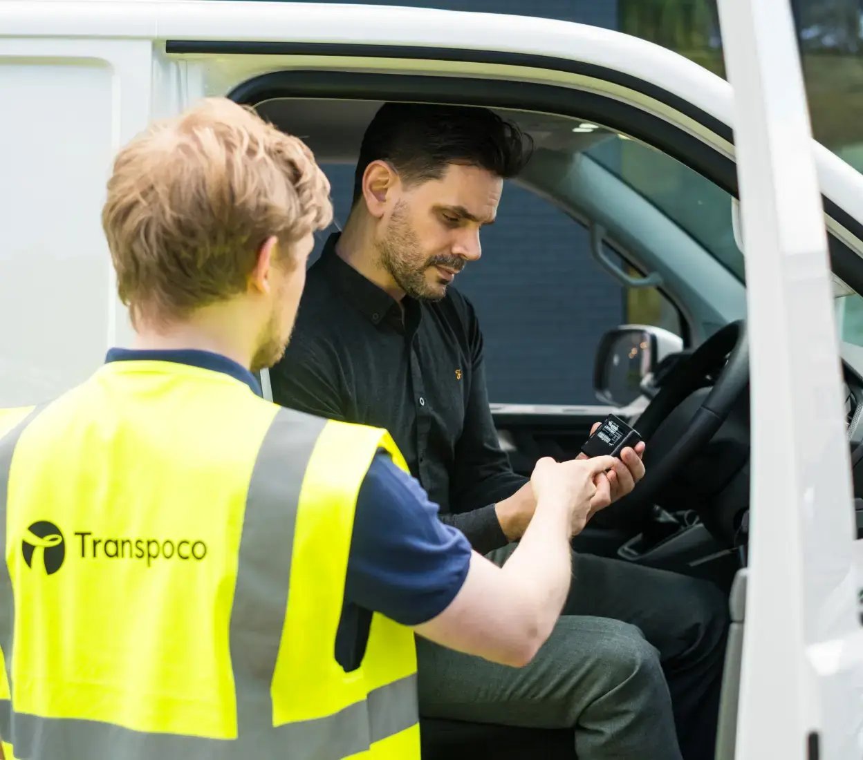 Transpoco employee in a high-vis jacket showing a driver how to use telematics equipment